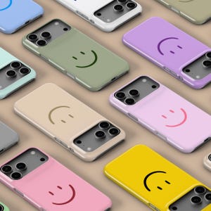 Könnte beinhalten: Eine Auswahl an farbenfrohen Handyhüllen mit einem Smiley-Gesicht-Design. Die Hüllen sind in verschiedenen Farben erhältlich, darunter Blau, Grün, Beige, Lila, Rosa und Gelb. Jede Hülle hat einen Kameraausschnitt.