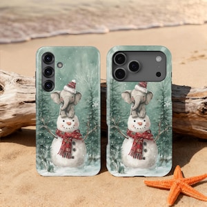 Könnte beinhalten: Zwei Handyhüllen mit Wintermotiv. Jede Hülle zeigt einen Schneemann mit rotem Schal und einen Baby-Elefanten mit Weihnachtsmütze. Der Hintergrund zeigt eine verschneite Waldszene.
