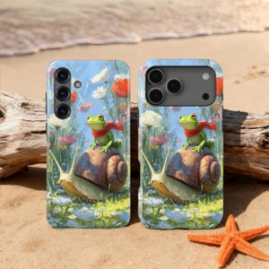 May include: Two phone cases with a whimsical design. Each case features a green frog wearing a red scarf riding on a snail, set against a backdrop of flowers and a blue sky. The cases are on a sandy surface with a starfish.