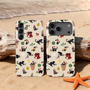 May include: Two phone cases with a repeating pattern of black cats wearing Santa hats, coffee cups, gifts, and ornaments on a beige background. The cases are on a sandy beach with a starfish and driftwood.