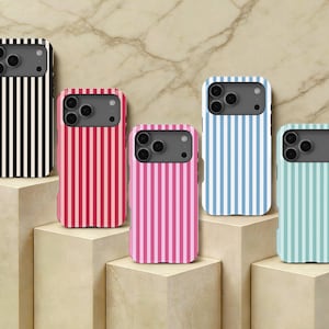 以下が含まれることがあります： 黒、赤、ピンク、水色、ミントグリーンの縦縞模様のスマートフォンケース5点。各ケースには、3つのレンズ穴とフラッシュを備えたダークグレーのカメラ用切り抜きエリアがあり、段差のあるライトベージュのブロックの上に配置されています。