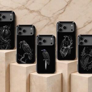 May include: Five black smartphone cases featuring detailed white line art illustrations of ravens. The designs include a raven on a branch with a key, a raven perched on a dagger with purple eyes, and a raven sitting within a crescent moon.