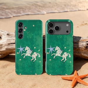 Puede incluir: Dos fundas verdes para teléfono con un diseño caprichoso que presenta un caballo blanco, una estrella azul y una luna creciente. Las fundas están decoradas con pequeñas estrellas. Las fundas están en una playa de arena con una estrella de mar y madera flotante.
