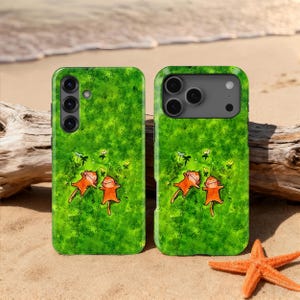 May include: Two green phone cases featuring a cartoon illustration of two orange monkeys on a green grassy field with butterflies. The cases are on a sandy beach with a starfish and driftwood.