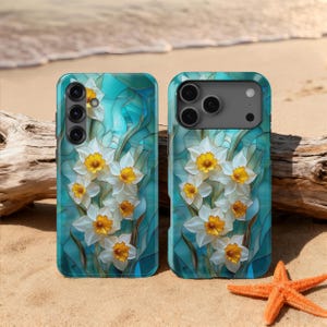 Puede incluir: Dos fundas para smartphone con un diseño floral de narcisos blancos con centros amarillos sobre un fondo turquesa. Las fundas están en una playa de arena con una estrella de mar y madera flotante.