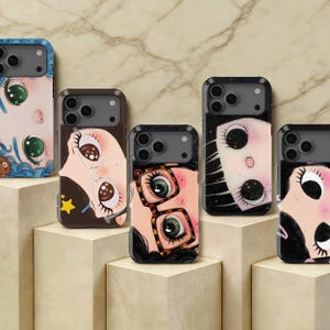 Può includere: Cinque cover per smartphone con illustrazioni stilizzate di volti con occhi grandi ed espressivi. I design includono vari colori di capelli, un personaggio che indossa occhiali tartarugati e un altro con pupille a forma di stella su sfondo marmorizzato.