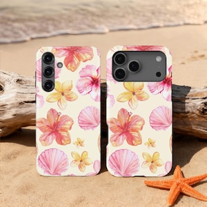Peut inclure: Deux coques de téléphone avec un fond crème, ornées de fleurs d'hibiscus et de coquillages aquarelles roses, oranges et jaunes. Les coques sont posées sur une plage de sable avec une étoile de mer et du bois flotté.