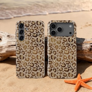 May include: Two phone cases with a leopard print design. The cases are tan with brown and gold spots. The cases are on a sandy beach with a starfish and driftwood.