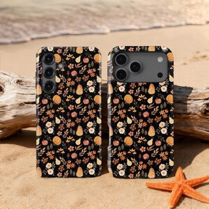 May include: Two black phone cases with a fall-themed floral pattern featuring pumpkins, pears, and flowers in shades of orange, yellow, and cream. The cases are displayed on a sandy beach with a starfish.