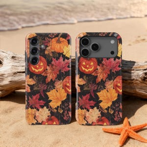 May include: Two phone cases with a Halloween theme. The cases feature a black background with orange pumpkins, red and yellow autumn leaves. The cases are on a sandy beach with a starfish and driftwood.