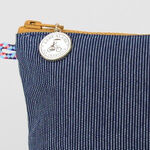 Puede incluir: Una bolsa de cremallera a rayas azules y blancas con un dije plateado que dice "Lady Alamo San Francisco" y presenta a una mujer montando una bicicleta con un paraguas.