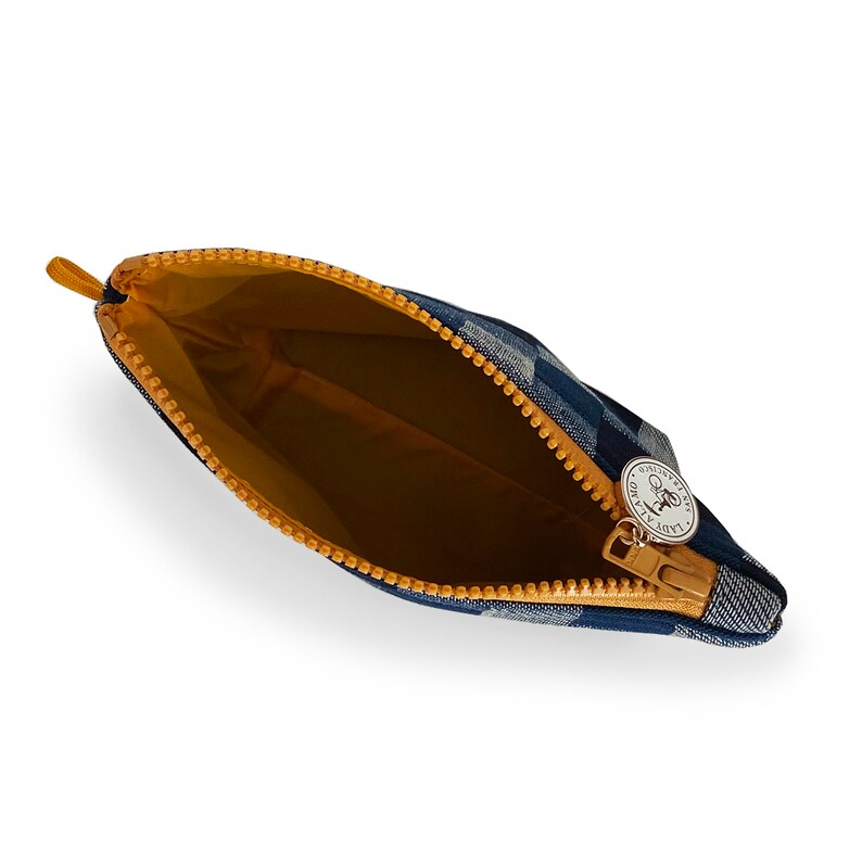 Puede incluir: Una bolsa con cremallera a cuadros azules y blancos con una cremallera amarilla y un dije plateado con el texto "Lady & The Tramp" en &eacute;l.