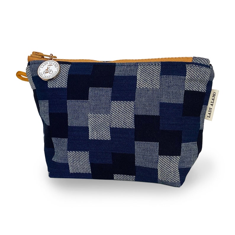 Puede incluir: Una bolsa de cremallera a cuadros azules y blancos con un tirador de cremallera de cuero marr&oacute;n. El tirador de la cremallera tiene un dije de metal con el texto "Lady Alamo San Francisco" y un gr&aacute;fico de bicicleta.