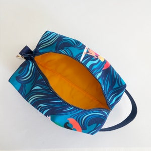 Op de afbeelding: Een blauwe en turquoise reistas met rits, met een kleurrijk golfpatroon en een gele binnenkant. De tas heeft een bovenste handvat.