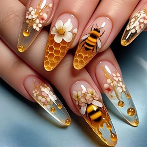 May include: Long, almond-shaped nails with a clear base feature intricate designs. Some nails showcase a honeycomb pattern, a bee, and white flowers. Others display delicate floral arrangements with gold accents and droplets.
