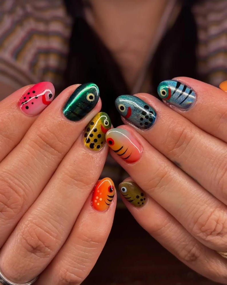 Puede incluir: Un conjunto de u&ntilde;as con dise&ntilde;os detallados de arte de u&ntilde;as que representan varios peces. Cada u&ntilde;a muestra una paleta de colores &uacute;nica que incluye rosa, verde met&aacute;lico, amarillo con puntos negros, azul, naranja y verde oliva, con ojos pintados.