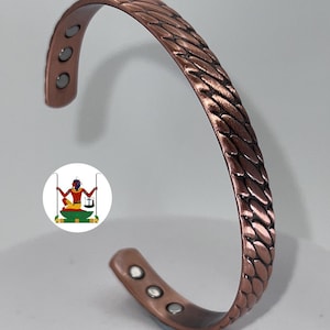 May include: A copper-coloured cuff bracelet featuring a textured, braided-style pattern on the exterior surface. The interior of the bracelet displays six small, circular silver-toned magnets embedded into the metal band at both ends.