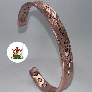 May include: A copper-coloured metal cuff bracelet featuring an embossed floral pattern on the outer surface. The interior of the open-ended band displays six small, circular silver-toned magnets embedded at both ends of the bracelet.