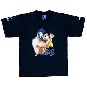 May include: Black t-shirt featuring a graphic of a masked wrestler in a blue mask and costume. The wrestler is in a fighting pose with the words "Blue Demon Jr." in blue and white. The shirt has a crew neck and short sleeves.