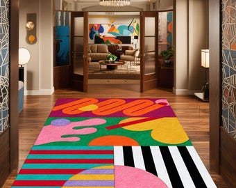 May include: A colorful area rug with an abstract design. The rug features sections of red, orange, green, pink, yellow, and black and white stripes. The rug is rectangular and placed on a hardwood floor.