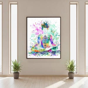 May include: A framed watercolor painting depicts a figure in a seated meditation pose. The figure is rendered in vibrant colors, with a focus on the chakras. Splashes of color surround the figure, creating a sense of energy and movement. The artwork is displayed on a neutral wall.