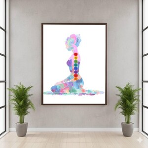 May include: A framed watercolor print of a person in a seated yoga pose. The figure is rendered in a colorful, abstract style, with a rainbow of hues. Seven chakra symbols are aligned along the spine. The artwork is displayed in a room with plants.