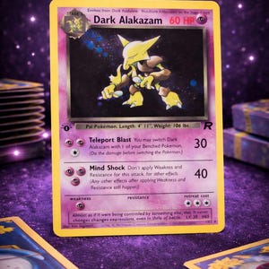 Może przedstawiać: Karta Pokémon Dark Alakazam z żółtym i fioletowym wzorem. Karta zawiera ilustrację żółtej istoty z brązowymi akcentami. Tekst karty zawiera "Dark Alakazam 60 HP" i "Teleport Blast".