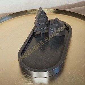 Könnte beinhalten: Ein schwarzes Dekotablett mit einem Miniaturhaus und einem Weihnachtsbaum. Das Haus hat Fenster und eine Tür. Das ovale Tablett liegt auf einer goldfarbenen Oberfläche. Der Text "SAUMSELIGES HAND" ist auf dem Tablett zu sehen.
