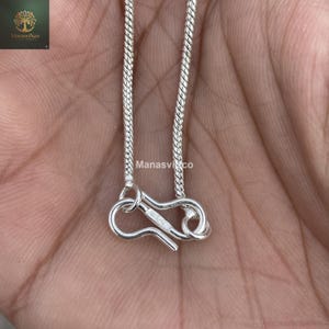May include: Close-up of a silver chain necklace with a hook clasp. The chain has a textured, woven design. The clasp is open, revealing the intricate details of the metalwork. The brand name "ManasviNco" is visible in the image.
