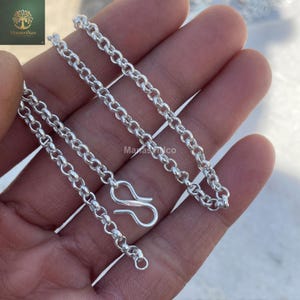 Puede incluir: Un collar de cadena de plata con un diseño de eslabones circulares. El collar tiene un cierre de mosquetón. La cadena se muestra en una mano.