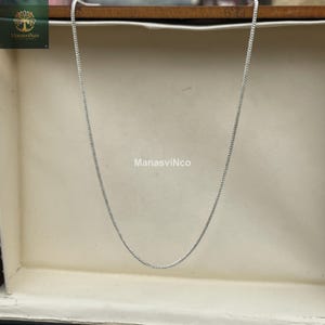 May include: A silver-colored chain necklace with a delicate, textured design. The necklace is displayed against a neutral background, with the brand name "ManasviNco" visible in the image.