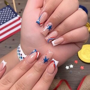 Puede incluir: U&ntilde;as manicuradas con tem&aacute;tica patri&oacute;tica. Las u&ntilde;as presentan un dise&ntilde;o de punta francesa con detalles en rojo, blanco y azul, incluyendo estrellas y rayas. Las u&ntilde;as son largas y de forma cuadrada, ideales para una celebraci&oacute;n.