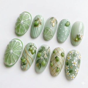 May include: A set of ten almond-shaped, green-themed artificial nails. Designs include lime slices, stripes, polka dots, gold accents, and floral patterns. The nails showcase a variety of textures and embellishments, creating a fresh and artistic manicure.