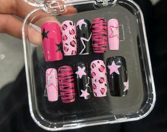 May include: A set of ten artificial nails in a clear plastic case. The nails feature various designs, including pink and black star patterns, leopard print, and zebra stripes. The nails are in shades of pink, black, and white.