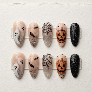 May include: A set of ten almond-shaped press-on nails featuring Halloween designs. The patterns include white ghosts, black bats, black spiderwebs, orange jack-o'-lanterns, and solid black glitter finishes on a nude, shimmering base.