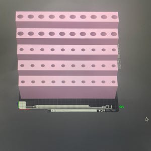 Puede incluir: Un organizador rosa de varios niveles con agujeros circulares espaciados uniformemente. El organizador está diseñado con una estructura escalonada, y los agujeros son consistentes en tamaño y colocación en cada nivel. El objeto se muestra sobre una superficie oscura.