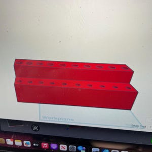 May include: A red, stepped, rectangular object with multiple circular holes. The object is labeled "Workplane" on a computer screen. The object appears to be a tool or a component for a larger project.