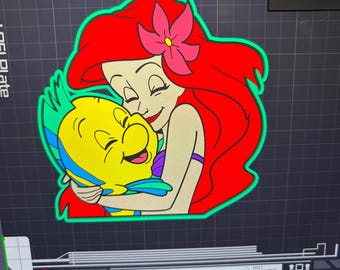 Può includere: Illustrazione colorata di Ariel de La Sirenetta che abbraccia Flounder. Ariel ha lunghi capelli rossi, un fiore rosa e un top viola. Flounder è giallo con pinne blu e verdi. L'immagine ha un contorno verde.