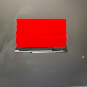 May include: A computer screen displays a 3D model of a red rectangular object. The object is composed of several stacked layers. The screen also shows various design tools and the text "Slice plate". The background is a dark gray.