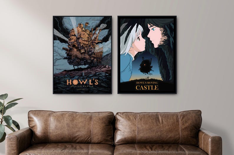 Puede incluir: Dos carteles enmarcados con ilustraciones de "El castillo ambulante". Uno muestra un castillo mec&aacute;nico, el otro representa a dos personajes. Los carteles se exhiben sobre un sof&aacute; de cuero marr&oacute;n.