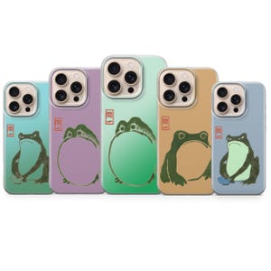 以下が含まれることがあります： 日本のスタイルのカエルのデザインが施された5つの携帯電話ケース。各ケースは、ティール、ラベンダー、グリーン、タン、ブルーの異なる色を特徴としています。カエルのイラストは黒と緑です。