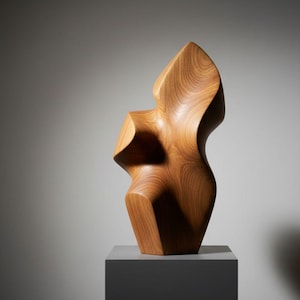 May include: A wooden sculpture with a smooth, flowing design. The sculpture is a light brown color and is displayed on a gray pedestal. The artwork has a unique, abstract shape with curved and angular elements.