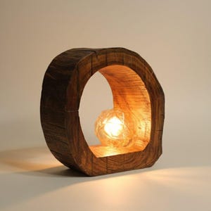 May include: A unique wooden table lamp with a circular frame. The lamp features a warm, glowing light source encased in a geometric glass sphere. The wood has a natural, textured appearance, adding a rustic touch to the design.