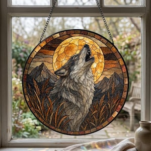 May include: A circular stained glass panel featuring a wolf howling at a large, golden full moon. The scene includes jagged mountain silhouettes and tall, amber-coloured grasses in the foreground, all framed by a dark, textured border.
