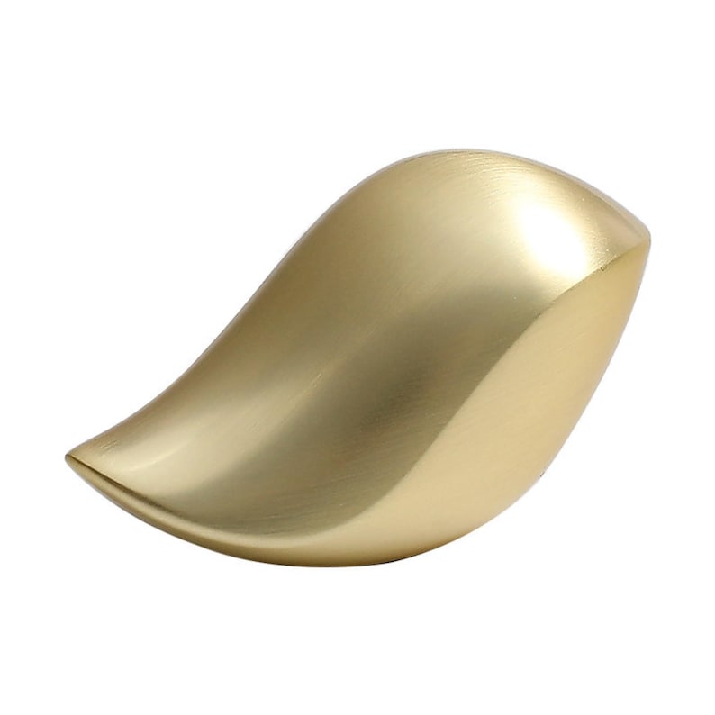 May include: A gold-colored, leaf-shaped decorative object. The smooth, curved surface reflects light, creating highlights and shadows. The object has a rounded, asymmetrical form, with a pointed tip and a wider base. The overall design is modern and minimalist.