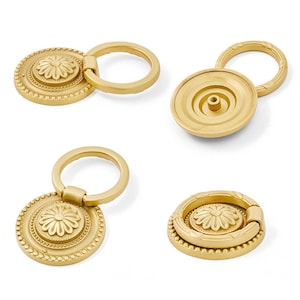 May include: Four gold-colored cabinet pulls with a floral design. Each pull features a circular backplate with a daisy-like center and a ring handle. The pulls are made of metal and have a matte finish, suitable for furniture hardware.