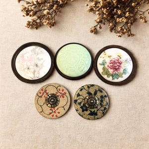 Puede incluir: Cinco posavasos decorativos de cerámica con diseños florales. Los posavasos presentan una variedad de colores, incluyendo blanco, verde, rosa y marrón. Cada posavasos tiene un patrón único, algunos con detalles en relieve y otros con flores pintadas.