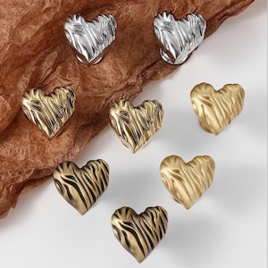 Pode incluir: Uma variedade de puxadores decorativos em forma de coração com vários acabamentos metálicos. Os puxadores incluem tons prateados, dourados e bronze, cada um com uma superfície texturizada e canelada. Ideal para decoração de casa ou artesanato.