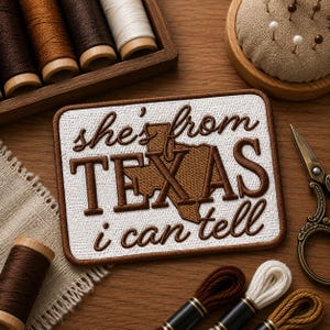 May include: Embroidered patch with the text "she's from TEXAS i can tell" in brown thread on a white background. The patch features a brown outline of the state of Texas. Sewing supplies, including thread spools and scissors, surround the patch.