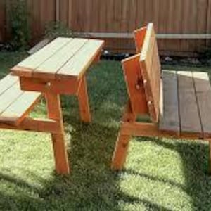 May include: A wooden picnic table and bench set. The table has a rectangular top and four legs. The bench has a backrest and four legs. Both are made of light brown wood and are outdoors on a grassy lawn.